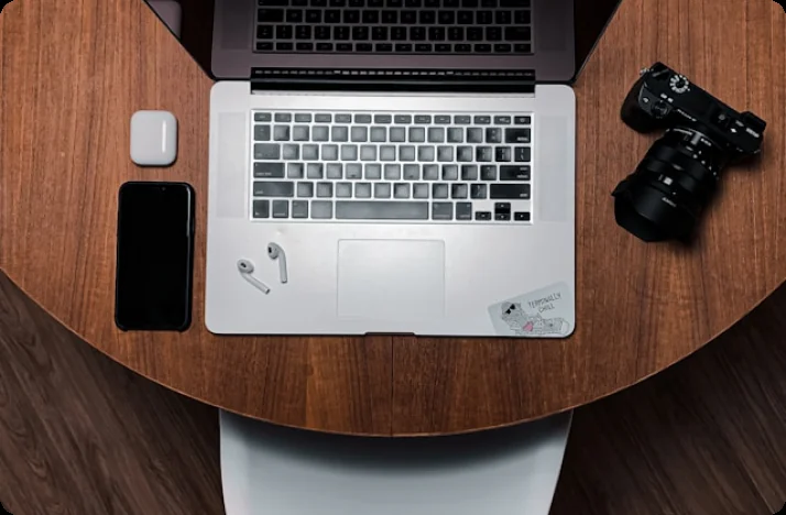 Laptop, camera and phone on a wooden desk